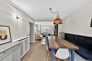 Una cucina moderna con un tavolo di legno, sedie bianche, un divano nero e una lampada a sospensione in rame.