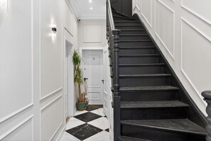 A hallway with a black and white checkered floor, a staircase with black steps and white trim, and a potted plant. - Studio, West Kensington + Hammersmith (Greater London)