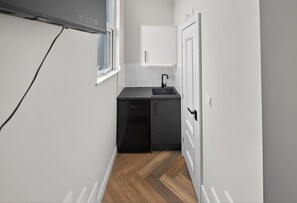 A narrow hallway with a kitchen area featuring a black countertop, a sink, and a black refrigerator. - Studio, West Kensington + Hammersmith (Greater London)