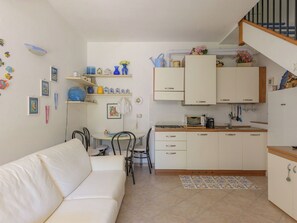 Eine kleine Küche mit weißen Schränken, ein Essbereich mit weißem Tisch und Stühlen sowie eine Treppe, die in einen oberen Bereich führt.