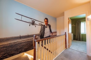 Ein Zimmer mit Wandmalerei eines Mannes im Anzug und eines Flugzeugs, einem Holgitter und einem Teppichboden.