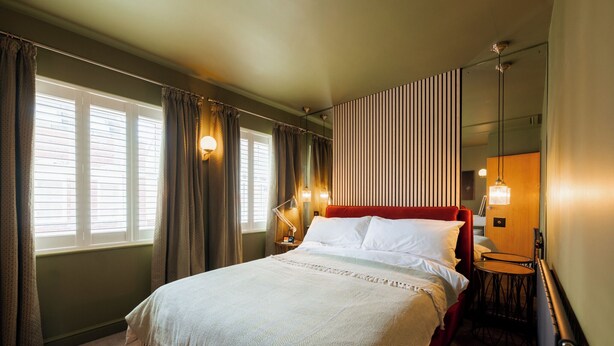 Una habitación de hotel con una cama grande, una mesita de noche, una pequeña mesa redonda y un espejo.