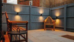 Un patio exterior con un banco de madera y una mesita, delimitado por una valla de madera con luces empotradas.