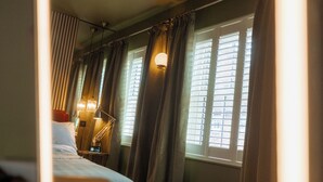 Quarto de hotel com uma cama, uma mesa de cabeceira com abajur e uma janela com persianas.