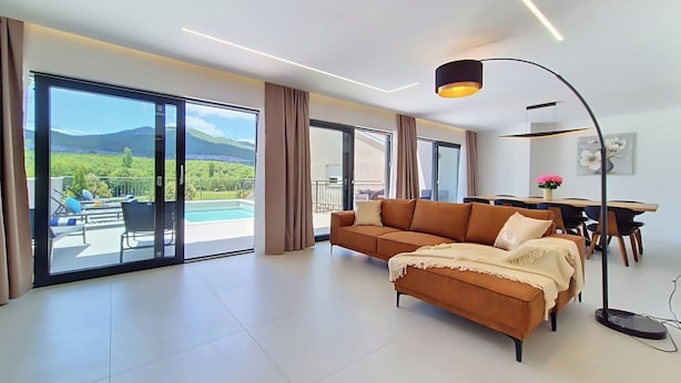 Una sala de estar moderna con sofá, mesa de comedor y vistas a una piscina y montañas.