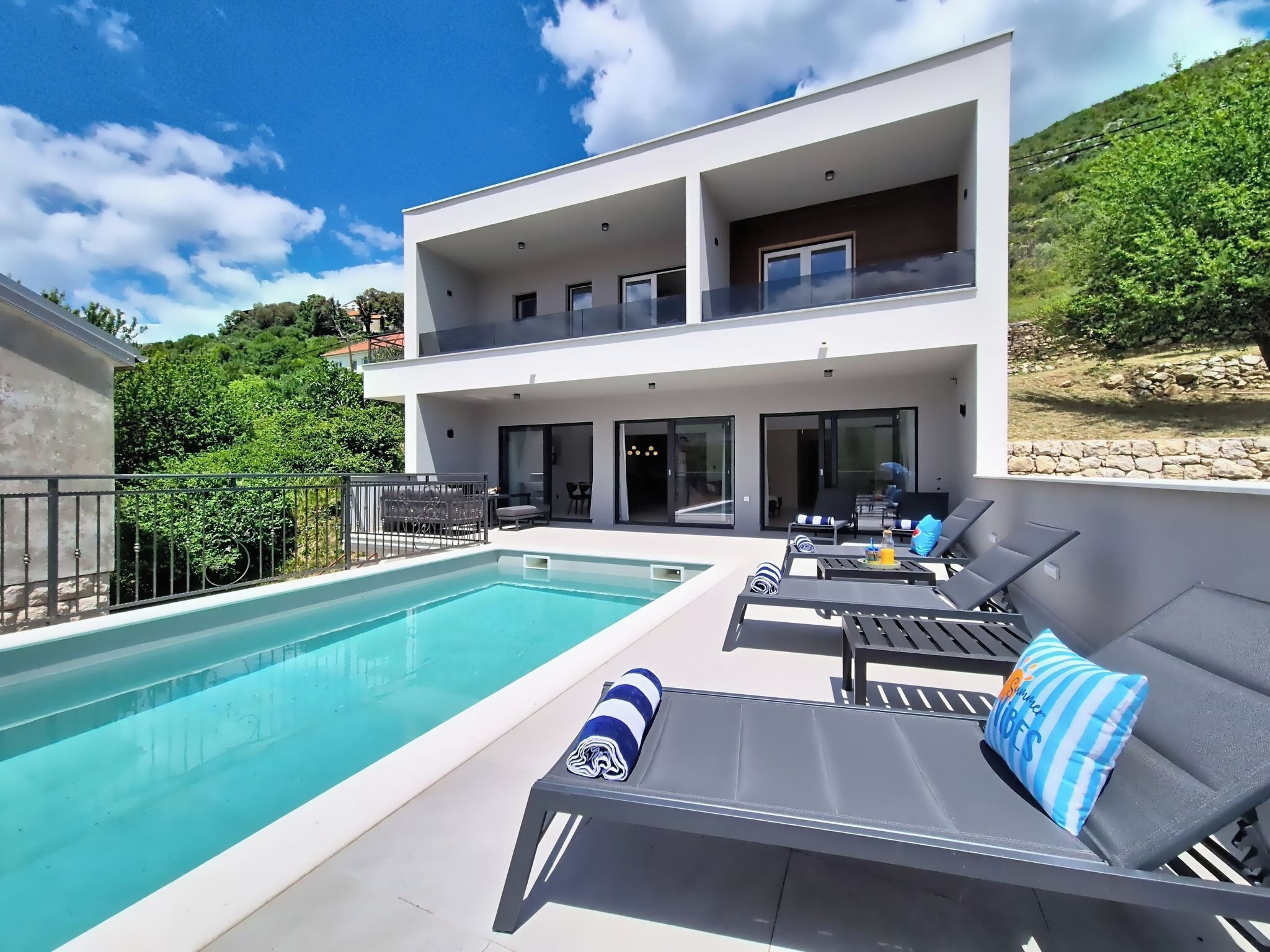 Uma casa moderna de dois andares com piscina, área de estar externa e vista para o verde ao redor.
