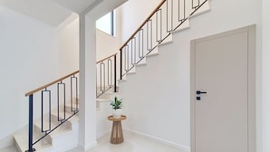 Una escalera moderna con barandilla de madera y barandillas negras, que conduce a una puerta con picaporte oscuro.