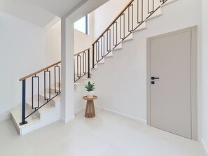 Eine moderne Treppe mit einem Holzhandlauf und schwarzen Spindeln, die zu einer Tür mit dunkler Klinke führt.