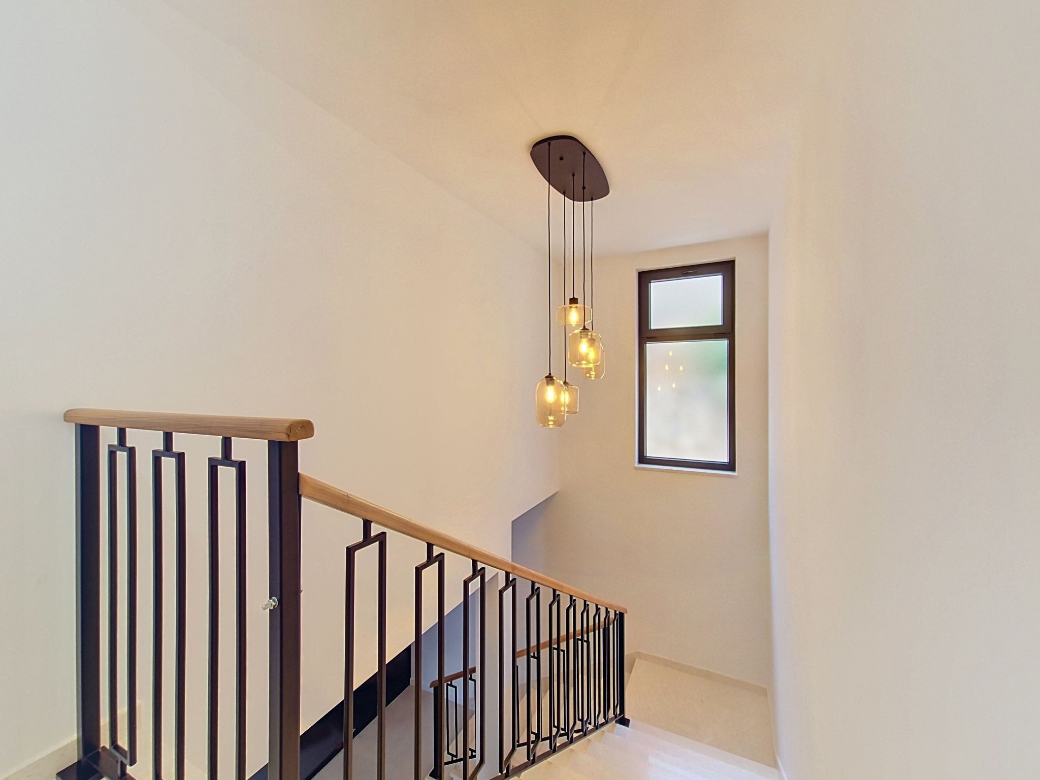 Eine Treppe mit Holzbalkon und schwarzen Metallspindeln, einer hängenden Leuchte und einem Fenster mit geätztem Glas.