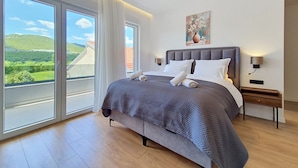 Un dormitorio con una cama grande, dos mesitas de noche, un cuadro y vistas al exterior.