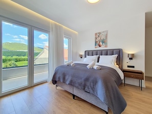 Ein Schlafzimmer mit einem großen Bett, zwei Nachttischen, einem Gemälde und Blick ins Freie.
