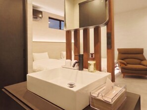 Un baño moderno con un lavabo blanco grande, un espejo y una mesita de noche con una caja de pañuelos.