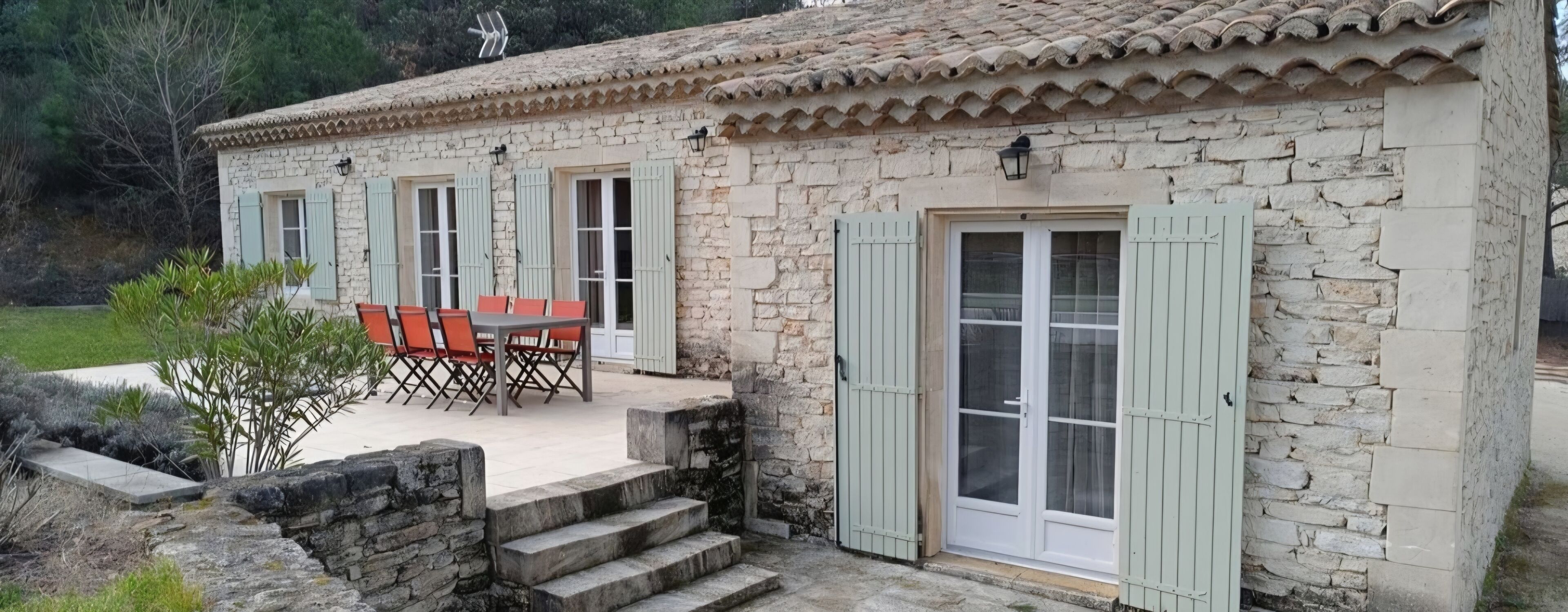 A stone building with a tiled roof, a patio with outdoor furniture, and a staircase leading to the entrance.