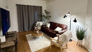 A living room with a brown leather sofa, a wooden coffee table, a TV, and a ceiling fan.