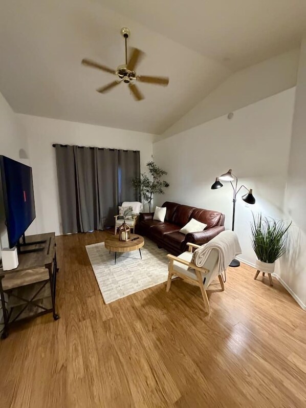 A living room with a brown leather sofa, a wooden coffee table, a TV, and a ceiling fan.