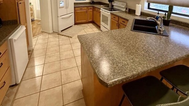 A kitchen with granite countertops, wooden cabinets, a refrigerator, microwave, stove, and a sink.