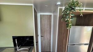 A compact kitchen with a stainless steel sink, a black stove, a wooden door, and a white refrigerator.