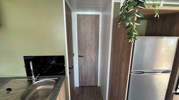 Een kleine keuken met een roestvrijstalen spoelbak, een zwart fornuis, een houten deur en een witte koelkast.