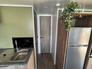 A compact kitchen with a stainless steel sink, a black stove, a wooden door, and a white refrigerator. - Cozy family chalet near a recreational lake, forest, and hiking trails (Gasselte)