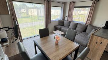 Een modern camperinterieur met een eettafel, zitplaatsen, een kitchenette en grote ramen met uitzicht op de omgeving.
