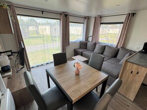 A modern RV interior with a dining table, seating, a kitchenette, and large windows offering a view of the outdoors. - Cozy family chalet near a recreational lake, forest, and hiking trails (Gasselte)