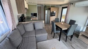 A modern living space with a sofa, dining table, chairs, kitchen area, and an air conditioning unit.