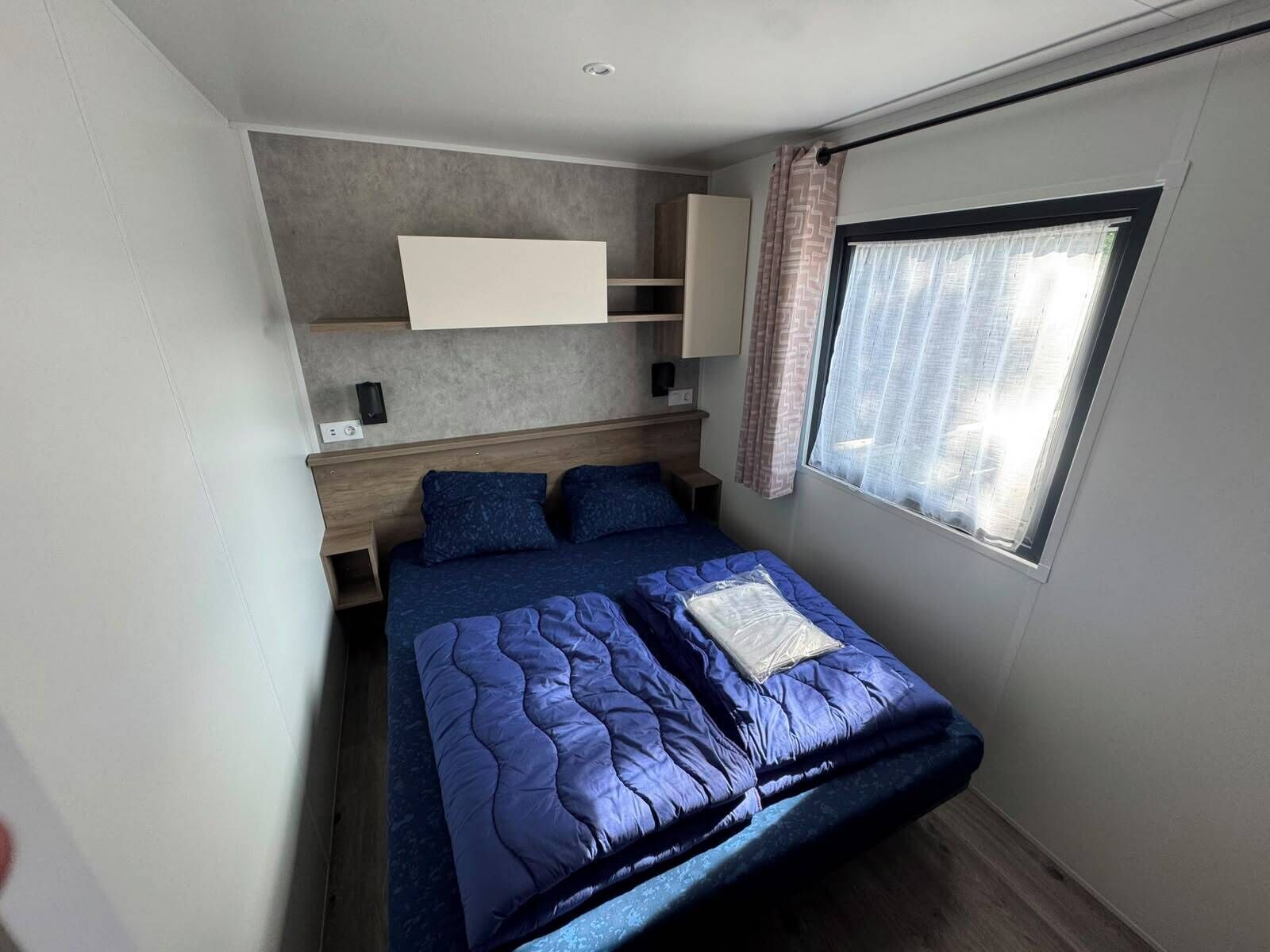 Een slaapkamer met een bed, een raam met gordijnen, een ingebouwde plank en een plafondlamp.