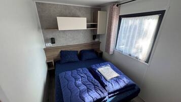 Een slaapkamer met een bed, een raam met gordijnen, een ingebouwde plank en een plafondlamp.
