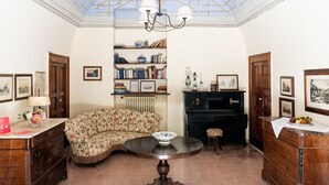 Um quarto com sofá curvo, mesa redonda, estante de livros, piano e quadros nas paredes.