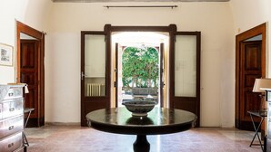Quarto com mesa redonda, portas de madeira e vista para um jardim através de uma porta.