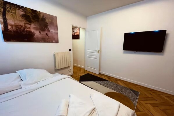Una camera da letto con un letto, un quadro, un termosifone, una porta e una televisione.