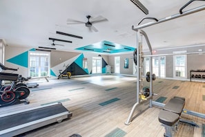 Un gimnasio con equipo de ejercicio, cinta de correr y ventilador de techo.