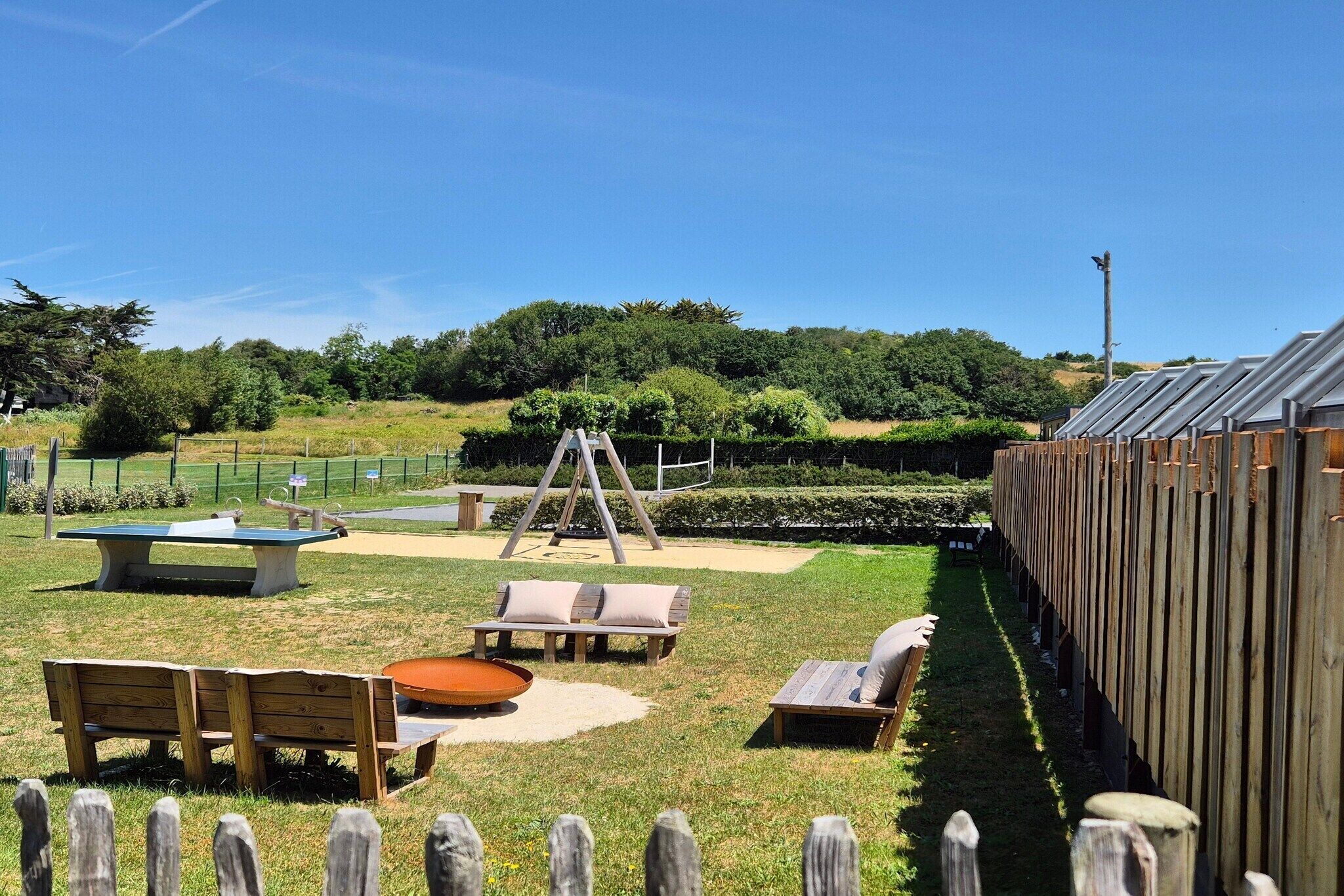 Un espacio al aire libre cercado con un conjunto de columpios de madera, una mesa de picnic y varias bancas.