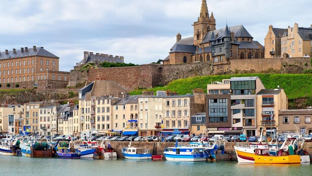 Een kustplaats met historische gebouwen, een opvallende kerk en een jachthaven met boten.