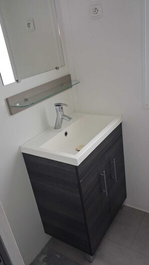 Ein Badezimmer mit einem weißen Waschbecken, dunklen Schränken, einer Glasablage und einem Spiegel über dem Waschbecken.