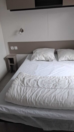 Ein ordentlich bezogenes Bett mit weißer Bettwäsche, ein kleiner Nachttisch und eine Wandleuchte.