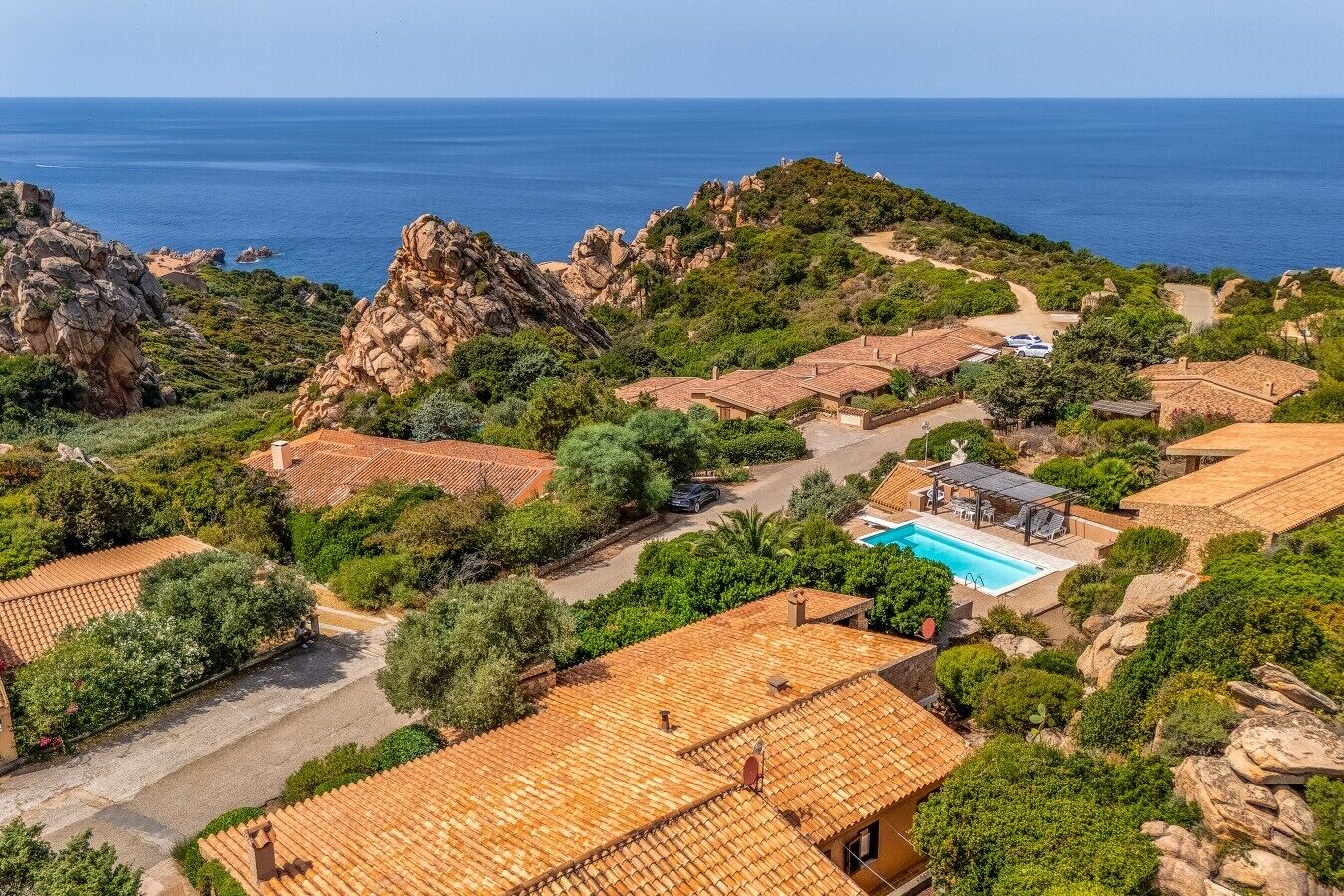 Une propriété située sur la côte, avec des bâtiments aux toits de tuiles rouges, une piscine et un terrain rocheux.