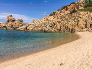 Ein Strand mit klarem Wasser, sandigem Ufer und felsigen Klippen.