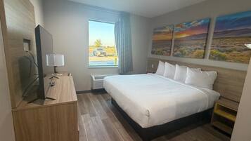 A hotel room with a large bed, a desk with a lamp, a flat-screen TV, and a window with a view of a parking lot.