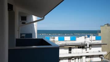 Un balcón con vista al mar y un edificio con toldos azules.