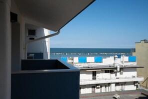 A balcony with a view of the sea and a building with blue awnings.