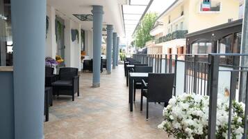 An outdoor café with tables and chairs, a tiled floor, and a glass ceiling.