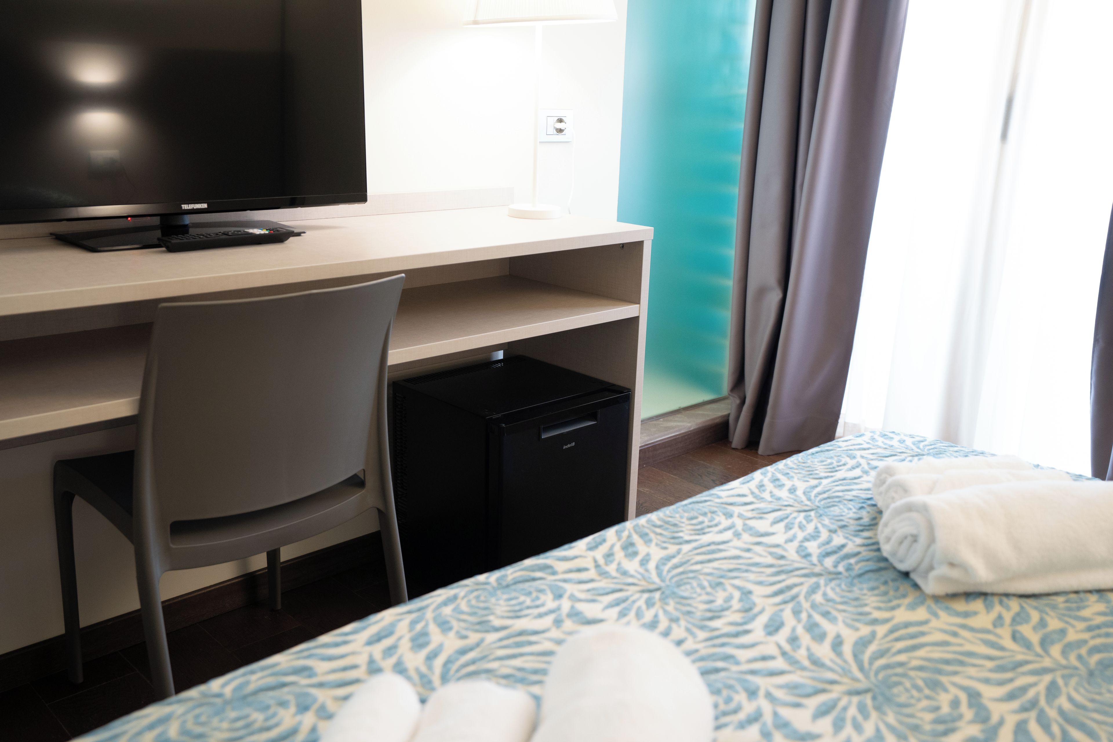 Ein Hotelzimmer mit einem Bett, einem Schreibtisch mit Fernseher, einem Sessel und einem kleinen schwarzen Gerät.