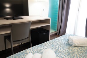 A hotel room with a bed, a desk with a television, a chair, and a small black appliance.