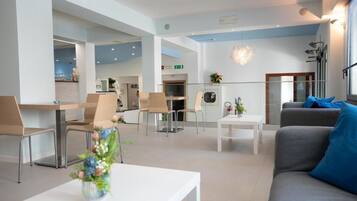 A modern hotel lobby with a reception desk, seating area, and a dining space.