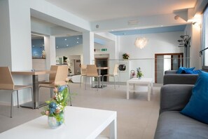 A modern hotel lobby with a reception desk, seating area, and a dining space. - Hotel Estense (Bellaria-Igea Marina)