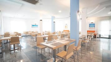 Un comedor amplio con mesas y sillas, un pilar grande y vistas al mar a través de las ventanas.