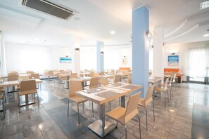 A spacious dining area with tables and chairs, a large pillar, and a view of the sea through the windows. - Hotel Estense (Bellaria-Igea Marina)