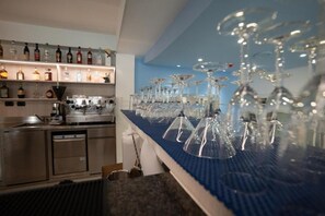 A bar area with a long counter, multiple bottles on shelves, and numerous glasses and wine glasses. - Hotel Estense (Bellaria-Igea Marina)