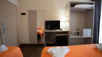 Une chambre d’hôtel avec deux lits, un bureau avec une télévision, une lampe, une armoire et une table de chevet avec une radio.